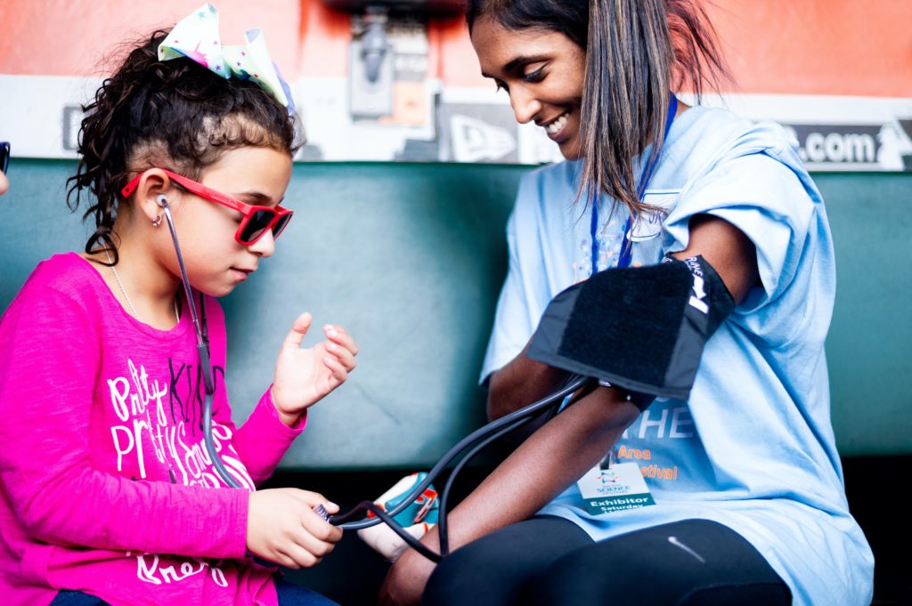 A UCSF medical student teaches a child how to check blood pressure using a blood pressure cuff.