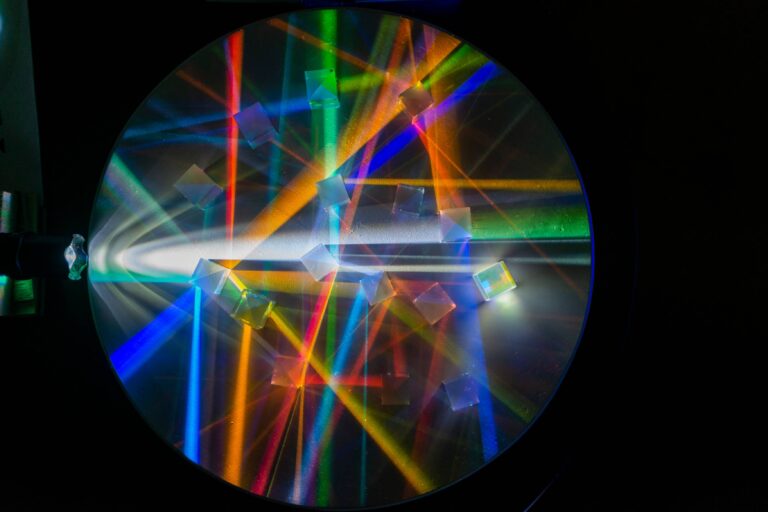Light shines through square prisms on a circular mirrored table revealing a rainbow of colorful beams