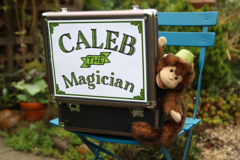 Stuffed monkey on a blue chair holding a box that reads CALEB the Magician.