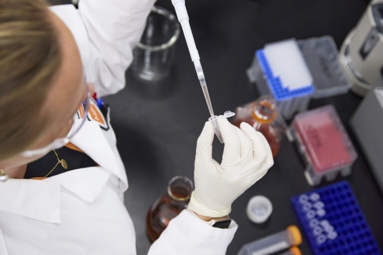 Scientist using a pipette to transfer liquid into a small vial.
